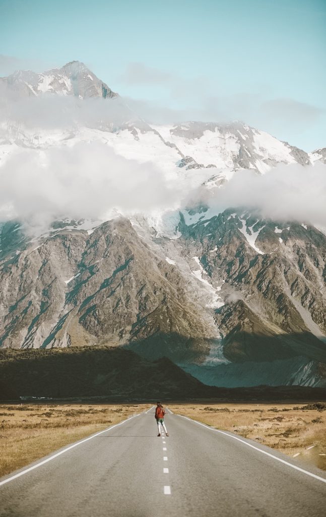 New Zealand Travel Guide | Person standing in the road taking in snow capped mountain view and blue skies, while traveling and visiting the South Island of beautiful New Zealand 