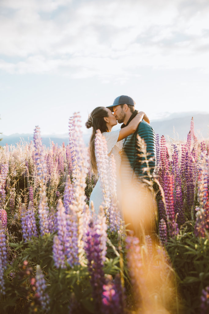 New Zealand Travel Guide | Couple kissing in the lupin fields near Lake Tekapo while traveling to New Zealand in the spring