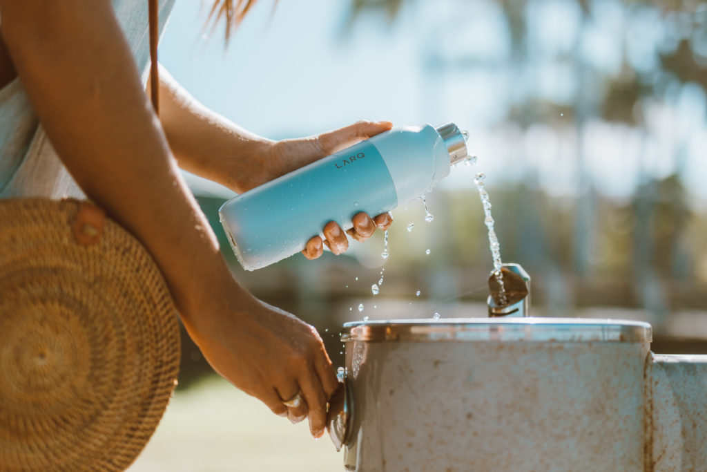 Filling a reusable water bottle from a water fountain. Ditch plastic water bottles when you travel with this portable disinfecting system. Sharing ways to reduce single-use plastic via @elanaloo + elanaloo.com