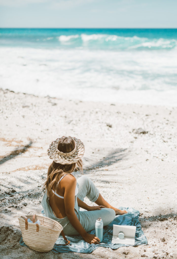 Woman on the beach holding LARQ reusable water bottle. Ditch plastic water bottles when you travel with this portable disinfecting system. Sharing ways to reduce single-use plastic via @elanaloo + elanaloo.com
