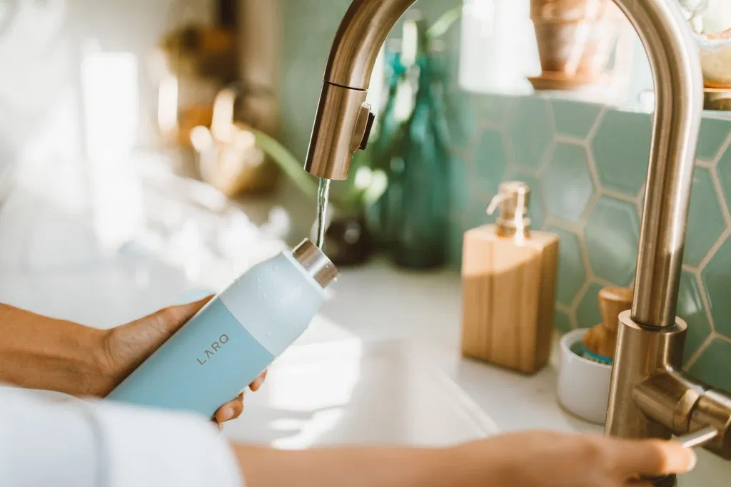 Filling a reusable water bottle in the sink. Ditch plastic water bottles with this portable disinfecting system. Sharing ways to reduce single-use plastic via @elanaloo + elanaloo.com